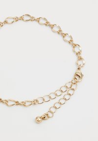 Pulseira de corrente de ouro com elos ovais e redondos mistos, fecho tipo lagosta e corrente de extensão ajustável terminando em uma pequena pérola de ouro.