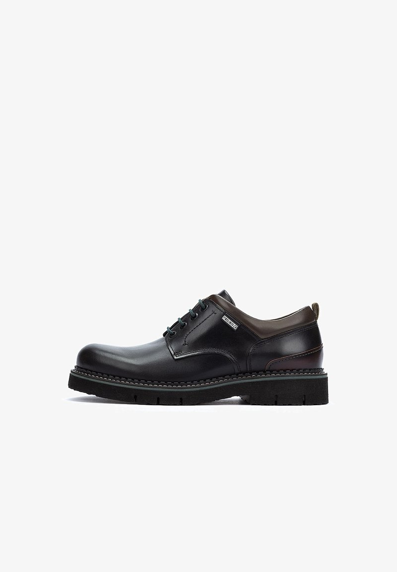 Zapato de cuero negro con acentos marrones, punta redonda, diseño de cordones, suela robusta, acabado texturizado y detalles de costura en contraste.