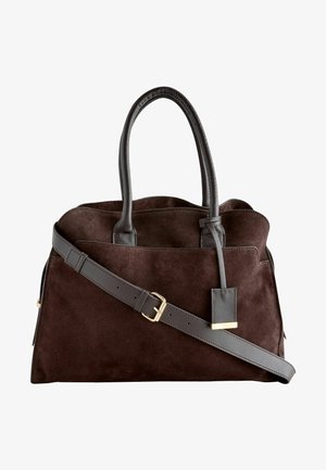 Sac en daim brun avec des anses en cuir noir. Doté d'une étiquette en métal doré et d'une bandoulière amovible pour plus de polyvalence.