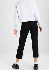 Světle modrá zkrácená mikina, černé džíny s vysokým pasem a rovnými nohavicemi, a černé tenisky s bílými detaily, pohled zezadu.