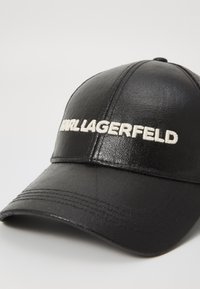 Čierna čiapka vyrobená z textúrovanej ekologickej kože, s bielou vyšívanou logom "Karl Lagerfeld" na prednej strane a zahnutým okrajom.