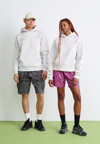 Lys grå hættetrøjer med kengurulommer, parret med mørke cargoshorts og lyserøde leopardprint shorts, begge toppet med sorte sneakers.