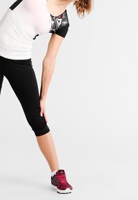 Idrottskläder bestående av en åtsittande vit och svart topp med korta ärmar, svarta capri-byxor och vinröda träningsskor med vita sulor.