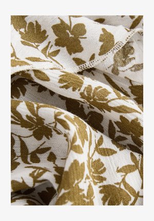 Tissu à motifs floraux en crème et vert olive, présentant un tissage doux et texturé avec des bords effilochés et des feuilles et fleurs entrelacées.