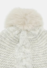 Cappello lavorato a maglia di colore grigio chiaro con un morbido pom-pom in pelliccia sintetica. Presenta un motivo testurizzato e un design a treccia sul corpo.