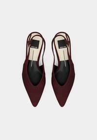 Ζευγάρι μπορντό μπαλαρίνες slingback με μυτερή μύτη, με μαύρα και μπεζ εσωτερικά πέλματα που φέρουν την ένδειξη "dolce vita", σε λευκό φόντο.