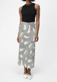 Sort ribbet tanktop parret med en lang hvid nederdel med sorte bølgede linjer. Fodtøjet er hvidt, med spidse tæer og rem detalje.