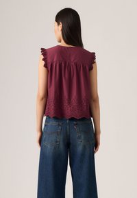 Top borgogna con maniche a cappuccino, bordo in pizzo e dettagli ricamati all'orlo, abbinato a jeans in denim a vita alta e gamba ampia.