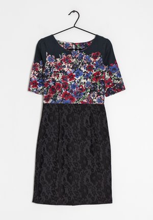 Robe avec le haut à motif floral en rouge, bleu et blanc, manches courtes foncées, et jupe noire texturée suspendue à un cintre noir.