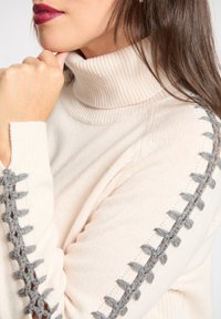 Kremowy sweter z golfem z szarymi dzianinowymi akcentami na rękawach, cechujący się miękką fakturą i prążkowanymi detalami na linii szyi i mankietach.