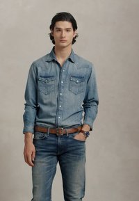 Camică din denim albastru deschis cu două buzunare pe piept, cu nasturi, asortată cu blugi din denim și o curea din piele maro. Design simplu, croi relaxat.