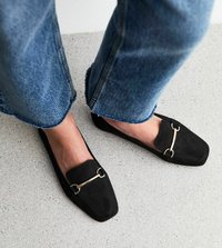 Zwarte suède loafers met een gouden accent, vierkante vorm en platte hak. Draagt met cropped denim jeans met rafelige zoom.