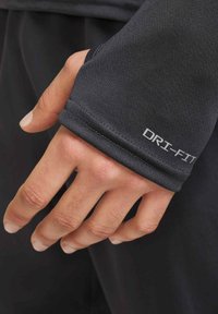 Schwarzer Dri-FIT-Sportbekleidungsbündchen mit glatter Textur, enger Passform und kleinem silbernem Logo in der Nähe der Naht. Teilweise sichtbare Hand.