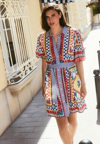Colorful short dress with puff sleeves, featuring a geometric pattern in red, blue, yellow, and green, cinched at the waist with a belt.