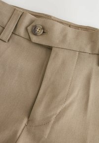 Pantaloni beige con frontale piatto, dotati di chiusura con bottoni e passanti per cintura. Il tessuto ha una texture liscia con cuciture pulite e sartoriali.