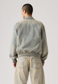 Τζιν μπουφάν σε ξεθωριασμένο ανοιχτό μπλε-γκρι χρώμα. Διαθέτει ριμπ μανσέτες και τελείωμα, μυτερό γιακά και άνετη εφαρμογή με λεπτομέρεια ραφής στην πλάτη.