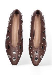 Chaussures en cuir marron avec un bout pointu, ornées de clous et d'accents métalliques. Texture lisse avec des détails décoratifs autour de l'empeigne.