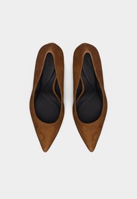 Καφέ σουέντ μπαλαρίνες με μυτερή μύτη και μαύρες μαξιλαρωτές εσωτερικές σόλες, τοποθετημένες δίπλα δίπλα σε λευκό φόντο.