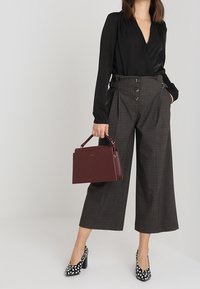 Černá dlouhá zavinovací blůza s dlouhými rukávy, kalhoty s vysokým pasem v kostkovaném vzoru, vínová kabelka a černé lodičky s puntíky. Čisté linie a dobře padnoucí střih.