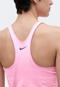 Άτομο που φοράει ροζ αθλητικό τοπ Nike με racerback, εμφανίζεται από πίσω και από τον ώμο, με έναν απλό φωτεινό φόντο.