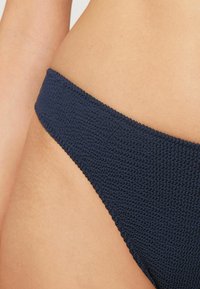 Námořnická modrá bikiny spodní část s texturovanou, tkanou látkou. Disponuje nízkým pasem a hladkými okraji, vhodná pro plavky.