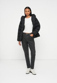 Čierna nafúknutá bunda s kapucňou, zapínanie na gombíky a rebrované manžety. Skombinovaná s šedými nohavicami s vysokým pásom a bielymi členkovými čižmami.