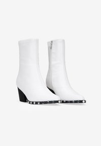 Bottes blanches en cuir avec un design épuré, bout pointu, et un accent noir orné de clous métalliques le long de la semelle.