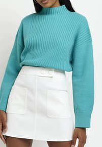 Tyrkysový žebrovaný svetr s vysokým výstřihem a dlouhými rukávy. Kombinován s bílou mini sukni, která má dvě přední kapsy a zapínání na patentky.