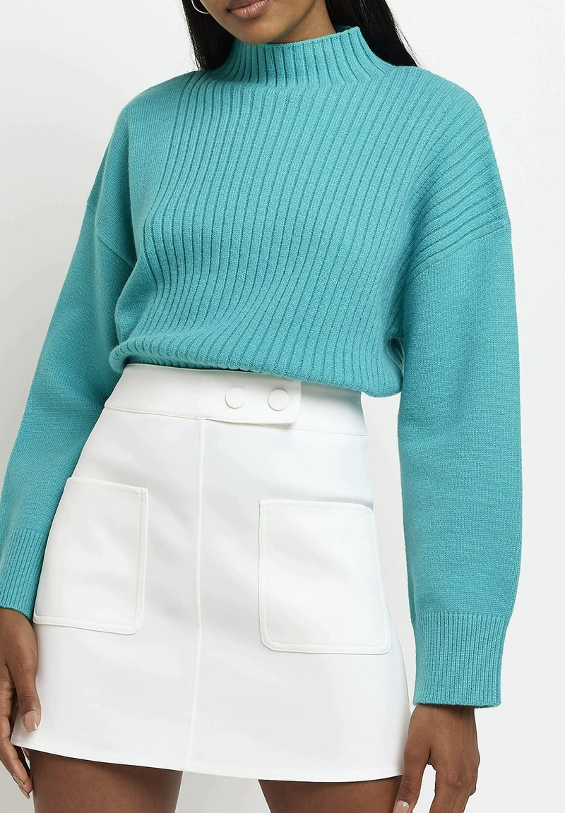 Tyrkysový žebrovaný svetr s vysokým výstřihem a dlouhými rukávy. Kombinován s bílou mini sukni, která má dvě přední kapsy a zapínání na patentky.