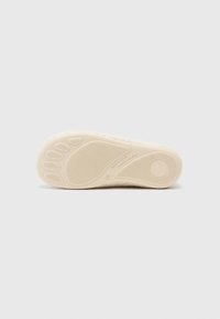 Crème-kleurige schoenzool met een getextureerd grippatroon, ronde vorm en geperste merktekens. Zacht, flexibel materiaal voor comfort.