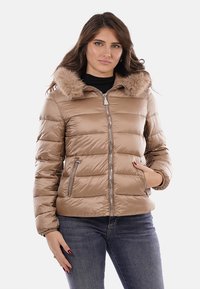 Giacca imbottita trapuntata color beige con collo in pelliccia sintetica, chiusura con zip, tasche laterali e silhouette aderente. Texture liscia e lucida.