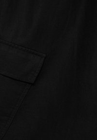 Tissu noir à texture lisse, présentant un design de poche plaquée et des détails de couture droite. Convient pour une tenue décontractée.