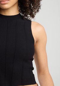 Black ribbed sleeveless top featuring a high neck, textured panels, and a fitted silhouette. Soft knit fabric emphasizes shape.