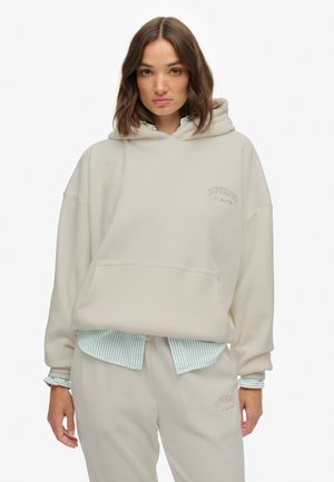 Hoodie beige clair en tissu doux avec une poche avant, comportant un petit logo "Superdry" brodé sur la poitrine. Coupe oversize.