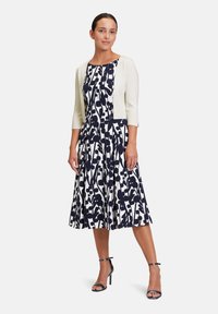 Navy and white floral patterned dress with a fitted bodice and flared skirt, paired with a cream cropped cardigan and black ankle strap heels.