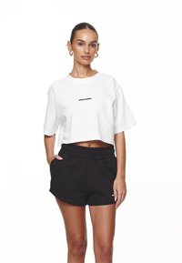 Hvid cropped t-shirt med "PEGADOR" trykt i sort, parret med sorte shorts med elastisk talje. Fremstillet af bomuldsmateriale, afslappet pasform, korte ærmer.
