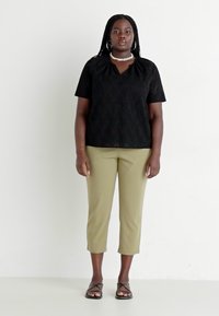 Svart blondetop med korte ermer og rund hals, kombinert med olivengrønne cropped bukser og svarte flate sandaler. Enkel, teksturert design.