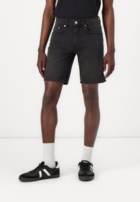 Svarte denimshorts med en tett passform, har fem lommer og sølvdetaljer. Stylet med svarte joggesko og hvite sokker.