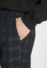 Pantaloni a quadri in un'elegante tonalità di blu scuro e verde, dotati di vita elasticizzata e tasche laterali. Il tessuto sembra morbido con una leggera trama.