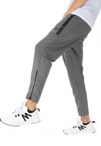 Šedé sportovní tepláky se zúženým střihem, černými akcenty, bočními zipy a texturovanou tkaninou, kombinované s bílými teniskami s černými detaily.