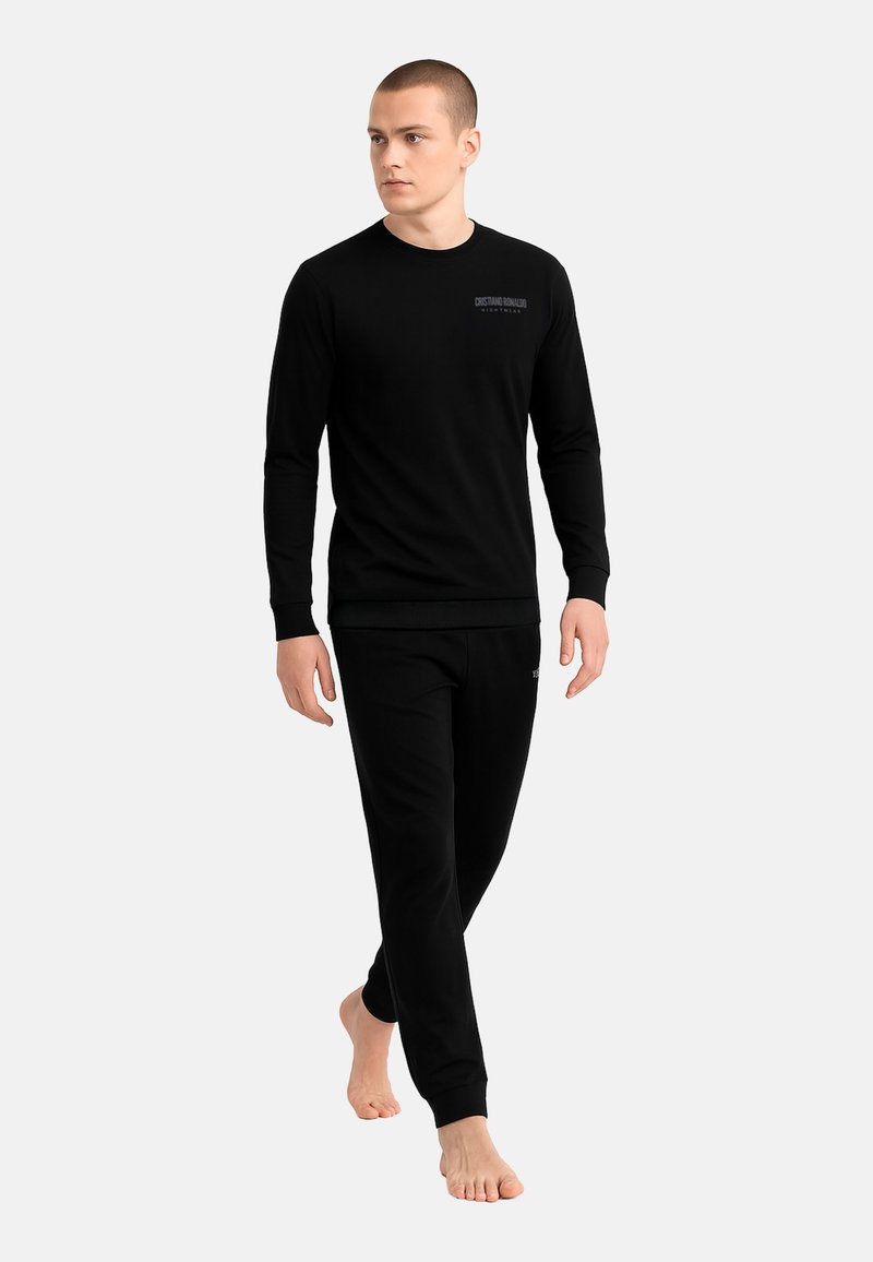 Maglietta nera a maniche lunghe e pantaloni della tuta abbinati, entrambi realizzati in tessuto morbido, con un logo discreto sul petto, polsini aderenti e fascia in vita.