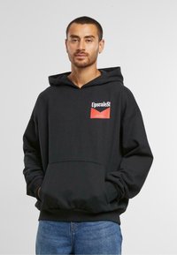 Felpa nera in cotone con tasca frontale, cappuccio con cordini e logo bianco e rosso sul petto. Texture morbida, vestibilità rilassata, design casual.