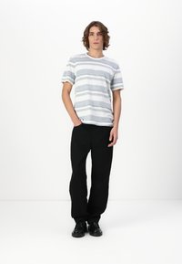 T-shirt rayé en gris clair, gris foncé et blanc, avec des manches courtes et un col rond. Associé à un pantalon large noir et des chaussures noires.
