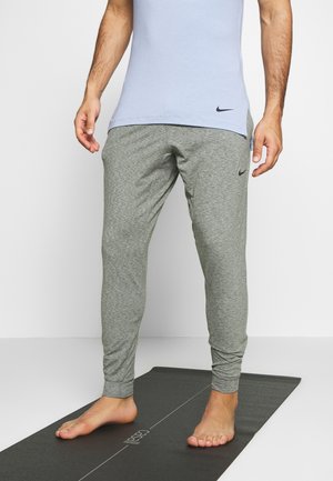 Personne debout pieds nus sur un tapis de yoga portant un t-shirt Nike bleu clair et un pantalon de jogging Nike gris.