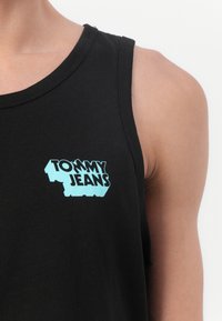 Fekete pamut ujjatlan felső kerek nyakkal és türkizkék "TOMMY JEANS" logóval. A szöveg vastag, geometrikus dizájnnal.