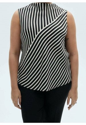 Persona con una camiseta sin mangas a rayas blancas y negras con líneas diagonales y verticales, combinada con pantalones negros sobre un fondo liso.