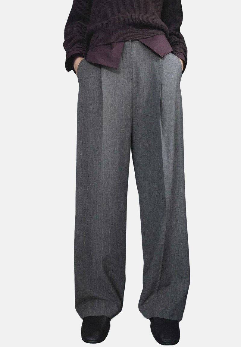 Grijze wijde broek met een streepjespatroon, voorzien van een gestructureerde stof en voorplooien, gecombineerd met een donkere, losse trui.