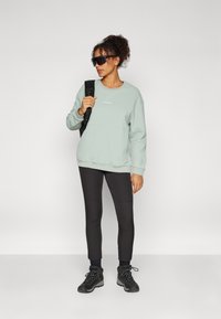 Mintgrønn genser med rund hals, ribbede mansjetter og kant; svarte leggings; og svarte turstøvler, komplettert med mørke solbriller.