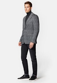 Szary blazer w kratę z wytłaczanymi klapami, z jedną zapięciem na guzik, bocznymi kieszeniami, połączony z dopasowanym czarnym golfem i czarnymi dżinsami. Czarne sneakersy.