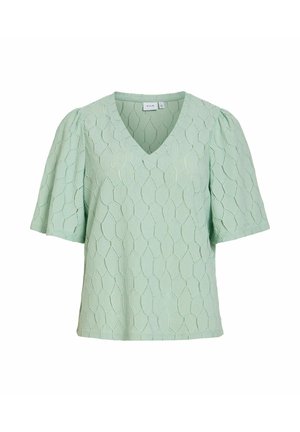 Lysegrøn bluse med korte ærmer, V-hals og subtilt geometrisk teksturmønster, løstsiddende pasform og let puffede ærmer.